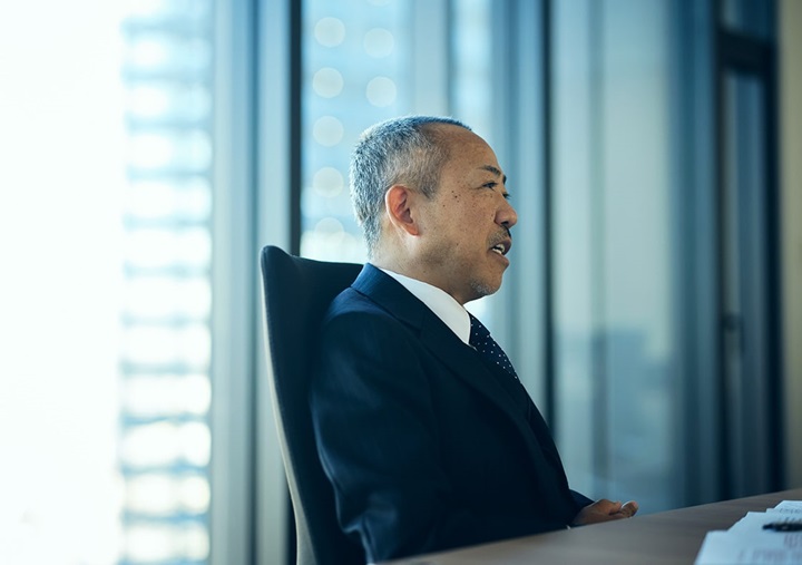 Tomohiro Sudo is sitting on a black chair and speaking.