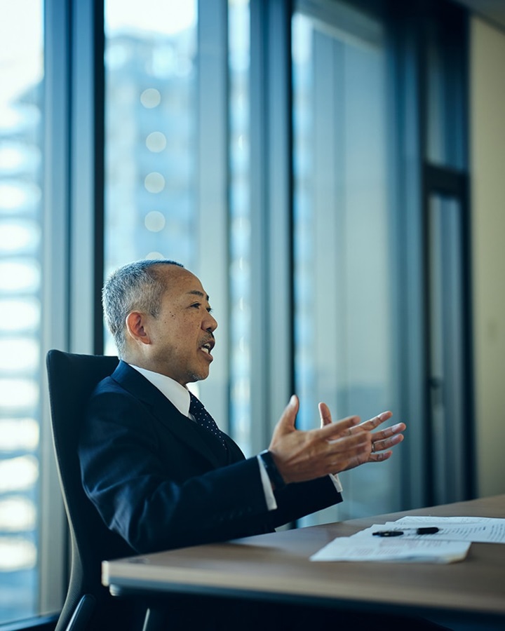 Tomohiro Sudo is sitting on a black chair and speaking.
